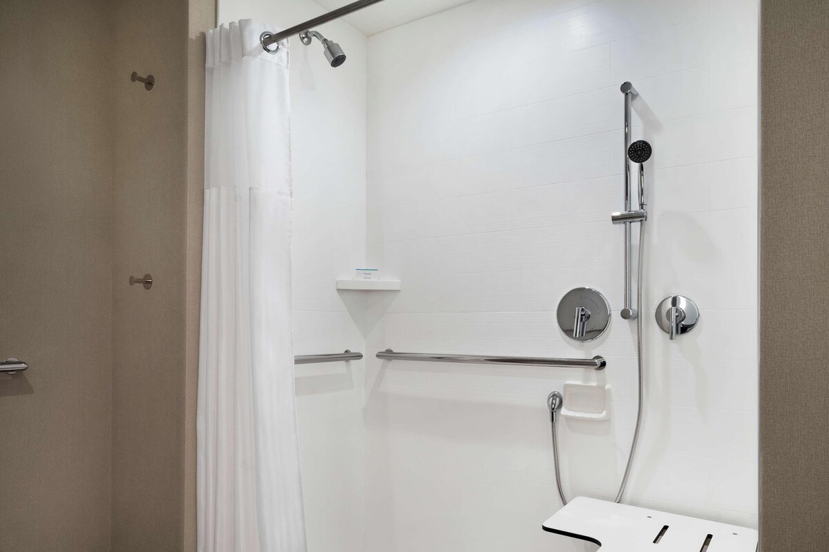 Un baño moderno con ducha de mano, grifo empotrado y barra de apoyo.