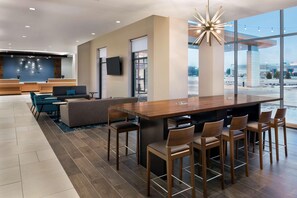 Eine moderne Hotelhalle mit Empfangstresen, Sitzgelegenheiten und einer großen Bar mit Hockern.