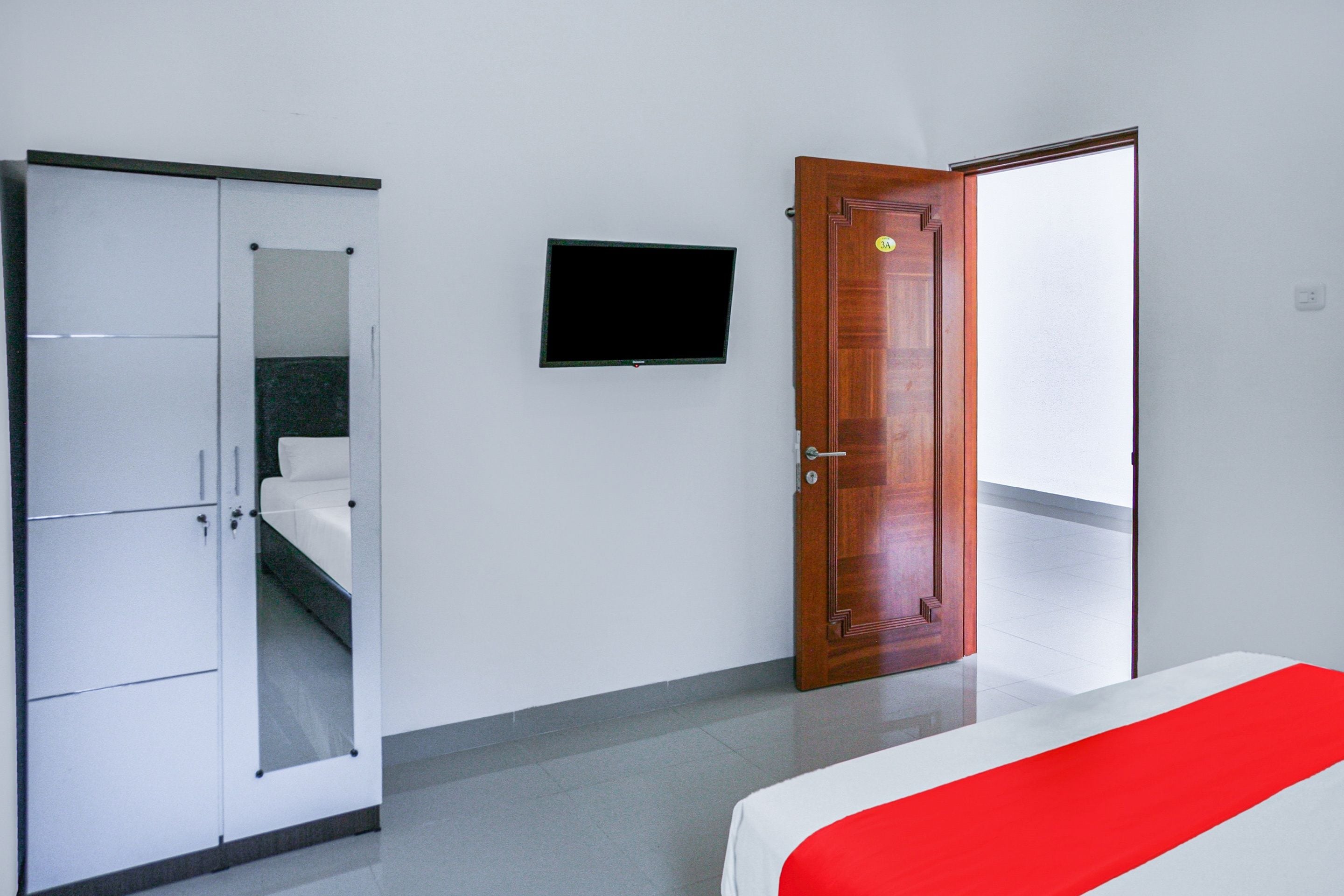 A bedroom with a bed, a wardrobe, a television, and a door leading to another room.