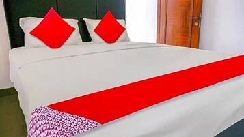 A bed with white bedding and two red pillows, a red throw blanket, and a wooden door in the background.