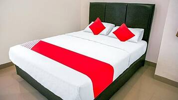 A bed with a white and red bedspread, a dark headboard, and two red pillows.