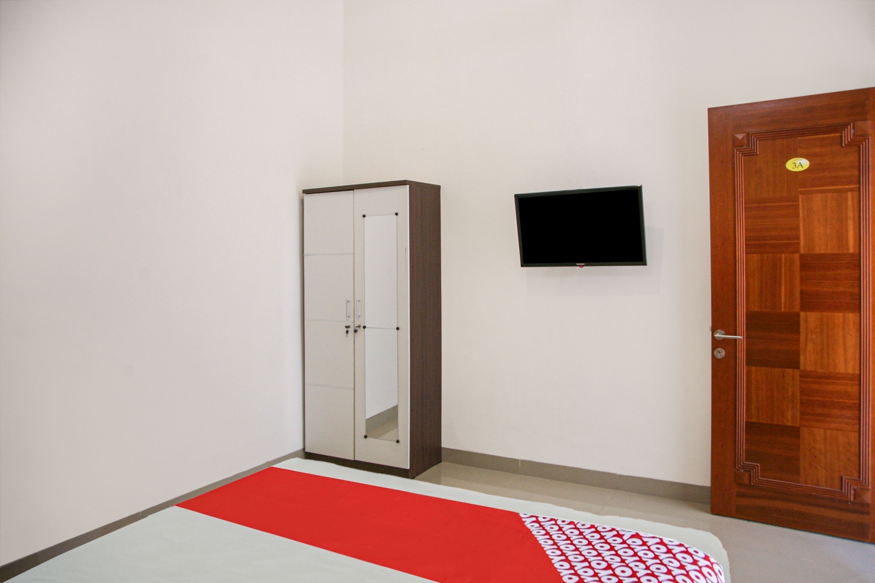 Habitació amb un armari, televisió penjada a la paret i una porta de fusta.