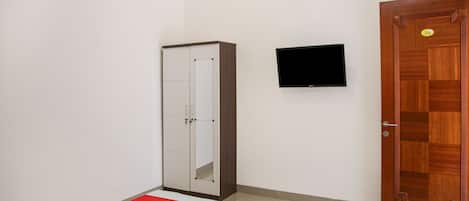 Una habitación con armario, televisor montado en la pared y puerta de madera.