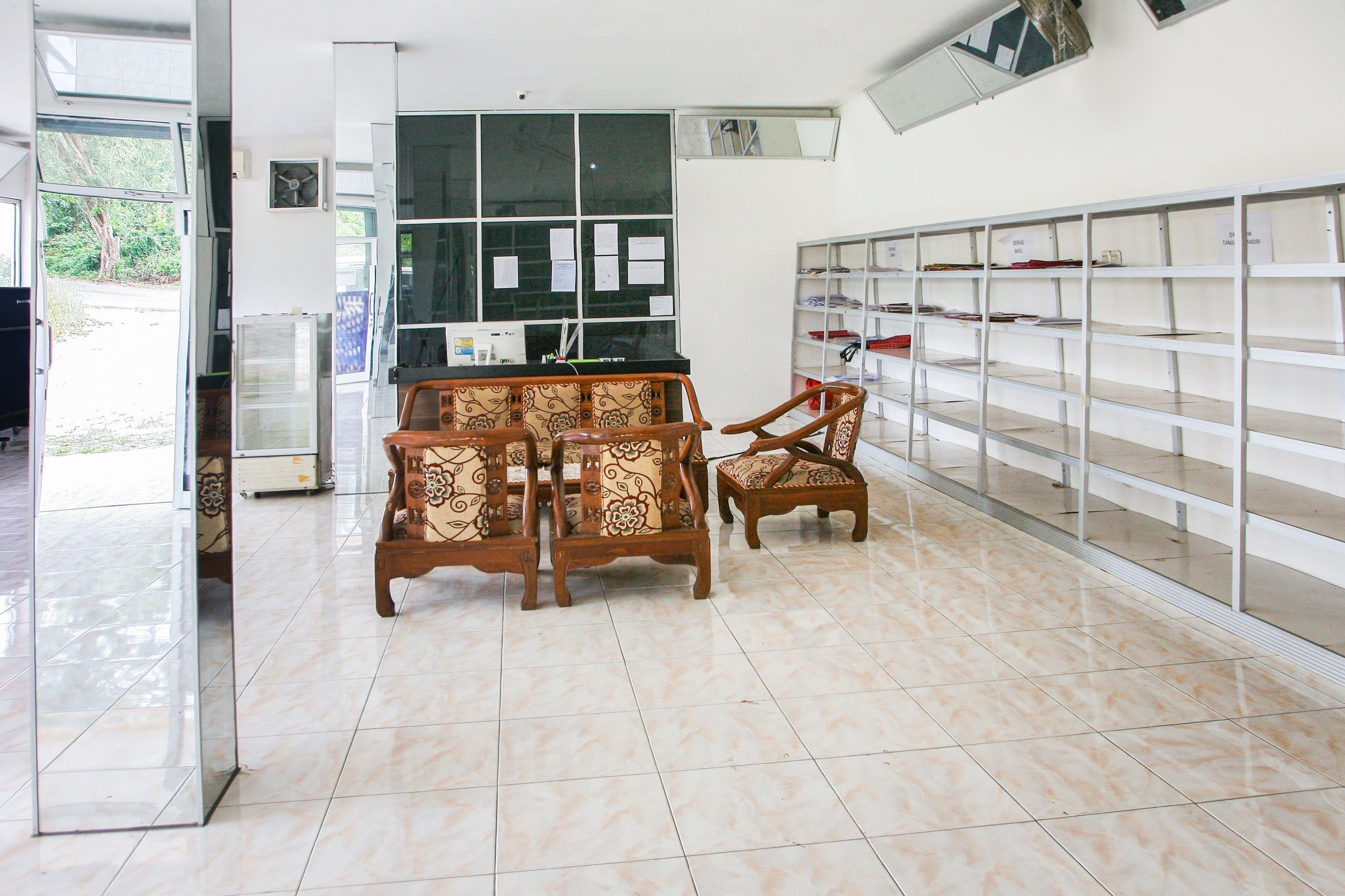 A room with a tiled floor, a wooden table with chairs, a window with papers, and a shelving unit with labeled compartments.
