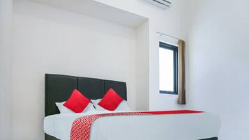 Ein ordentlich bezogenes Bett mit einer rot-weißen Tagesdecke, einem dunklen Kopfteil und zwei roten Kissen.
