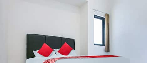 Una cama bien tendida con una colcha de cuadros rojos y blancos, un cabecero oscuro y dos almohadas rojas.