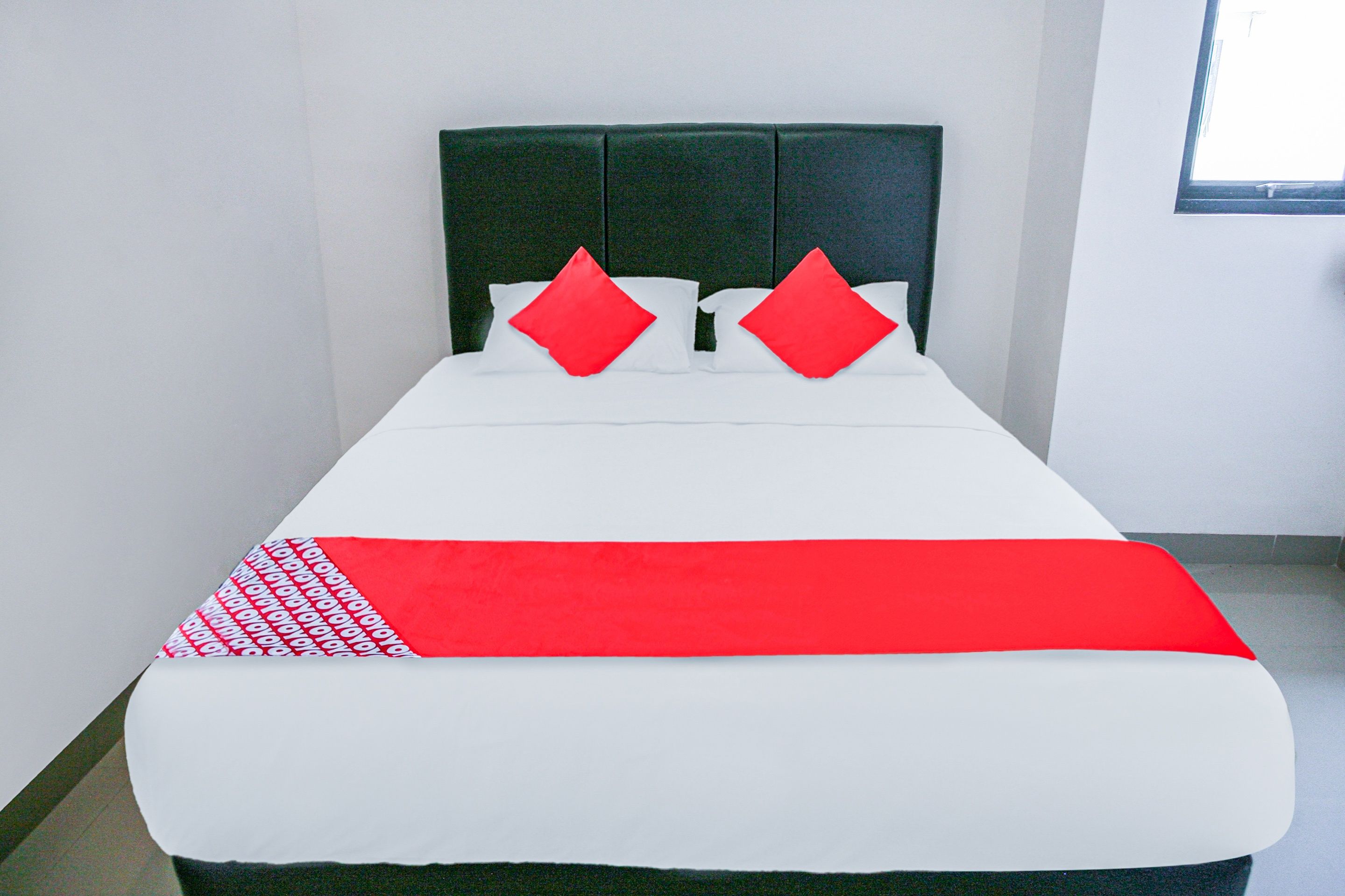 Una cama con una colcha blanca y roja, dos almohadas rojas y un cabecero verde en una habitación de hotel.