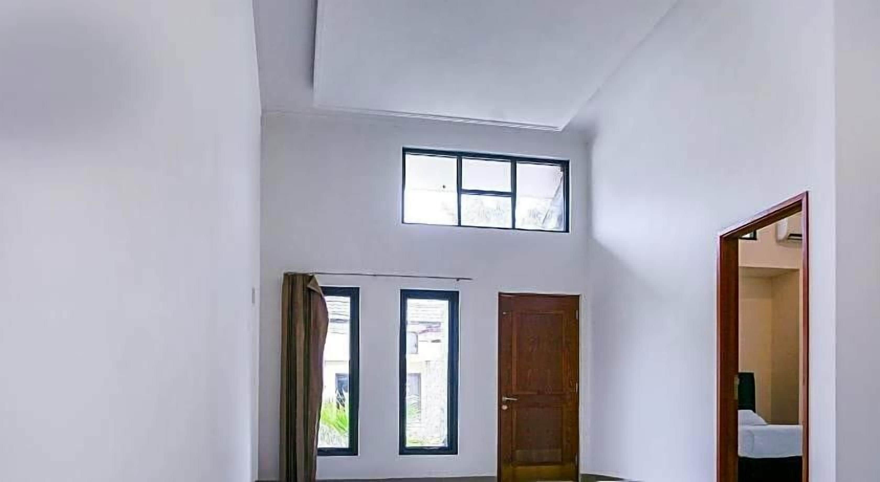 A room with a high ceiling, a wooden door, and two windows.