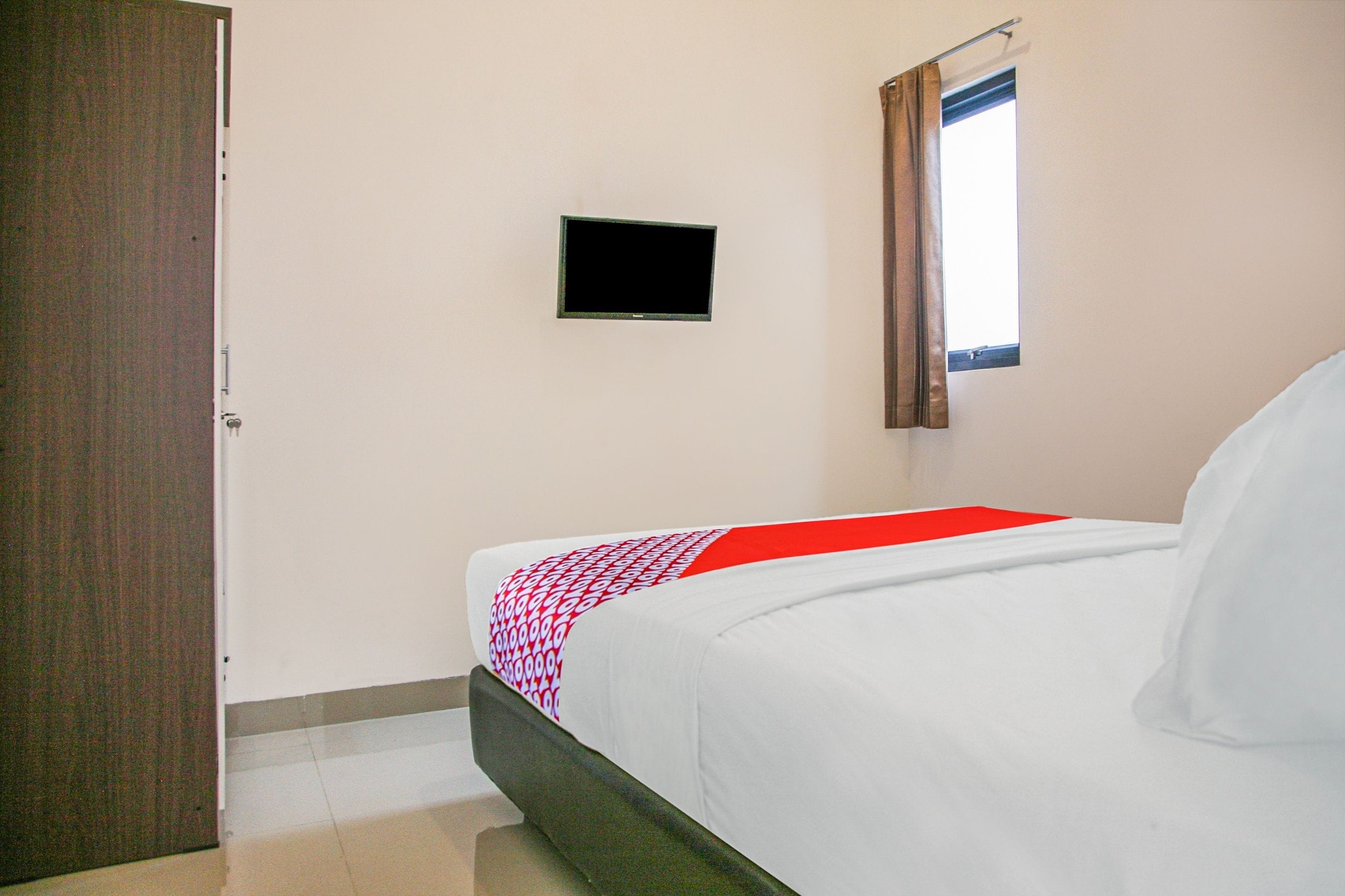 A bedroom with a bed, a television mounted on the wall, and a window with curtains.