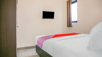 A bedroom with a bed, a television mounted on the wall, and a window with curtains.