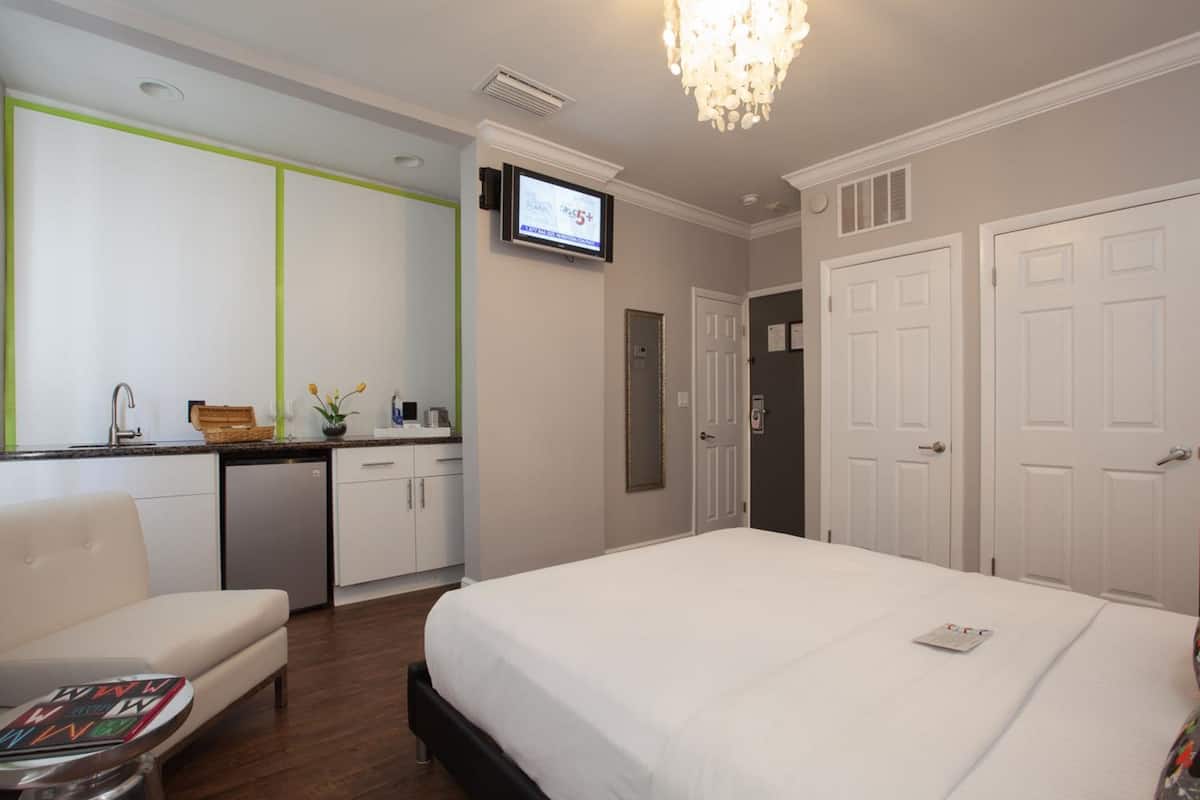 Quarto de hotel com cama, escrivaninha, cadeira, televisão e armário.