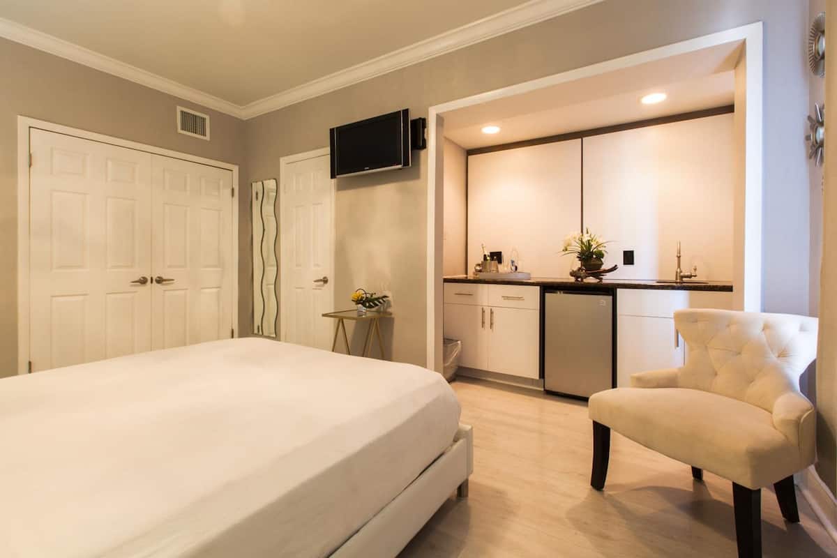Quarto com cama, poltrona, televisão, cozinha compacta e banheiro.