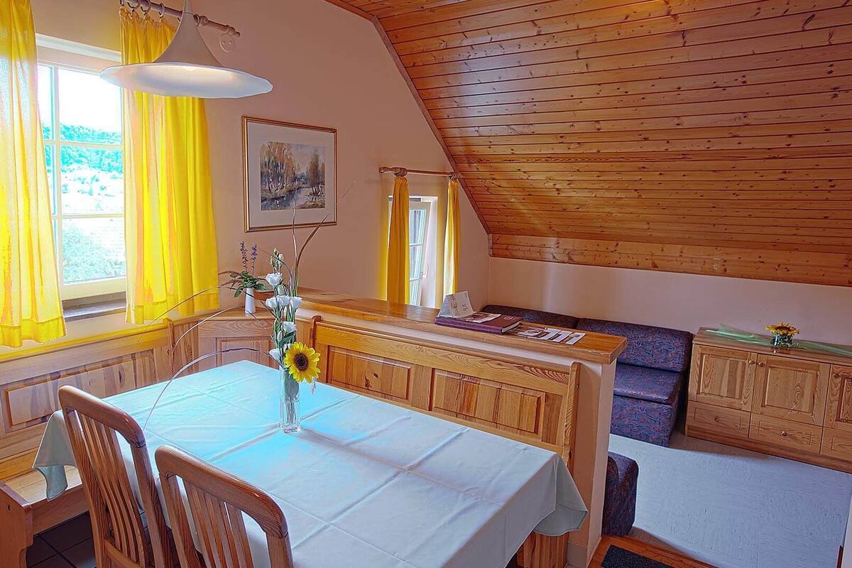 Ein gemütliches Zimmer mit Esstisch, Stühlen, einer Bank und einer Holzbalkendecke.