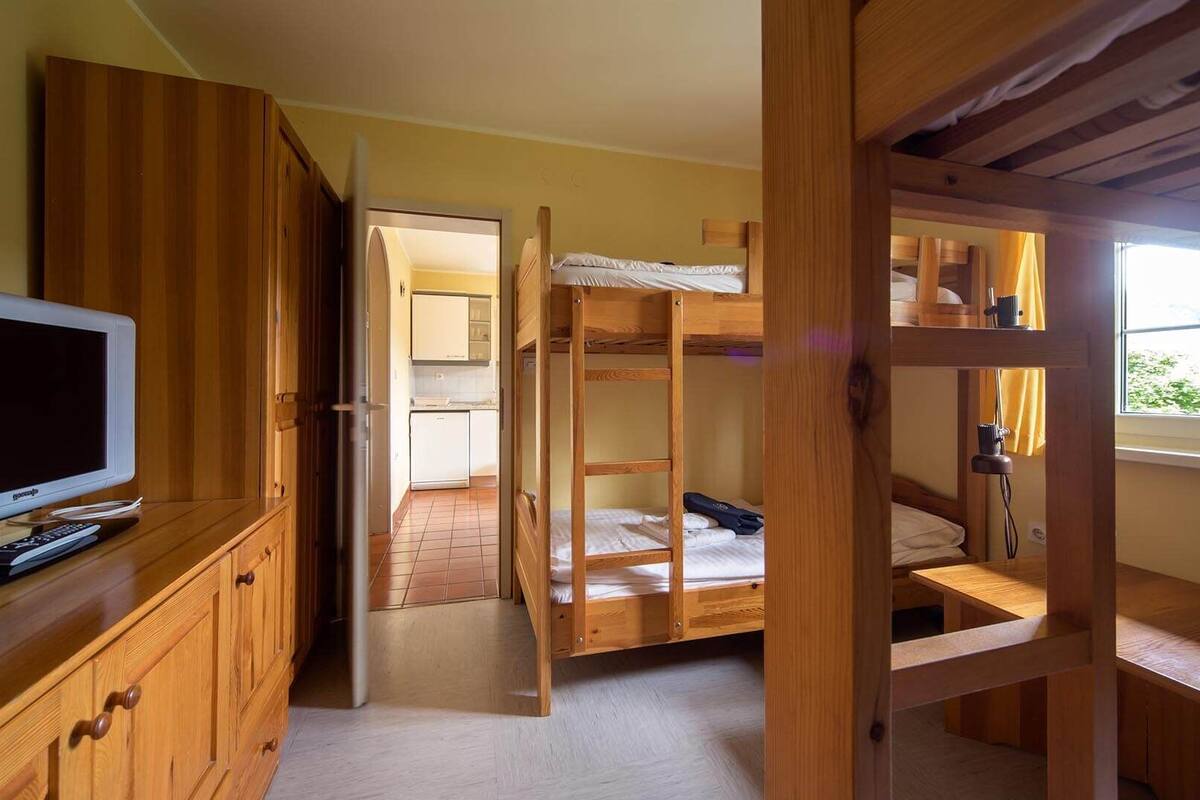 Ein Zimmer mit Etagenbett, Holzmöbeln, einem Fernseher und einem Fenster.