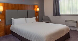 A hotel room with a large bed, wooden headboard, two wall-mounted lamps, a chair, a window with curtains, and a radiator. - The Magnum Hotel Sunderland Sure Collection By Bw (Sunderland)