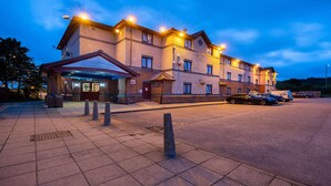 Um hotel de vários andares com entrada coberta, área de estacionamento e uma fileira de carros estacionados.