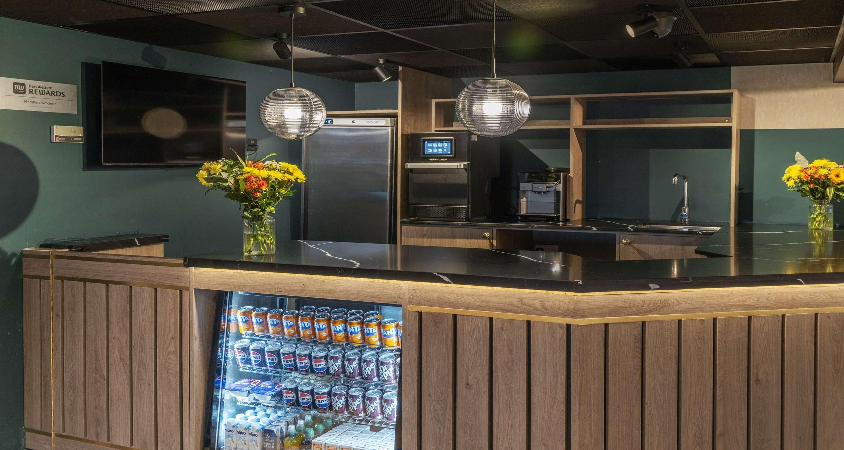 A bar area with a refrigerator stocked with beverages, a coffee machine, and two flower arrangements.