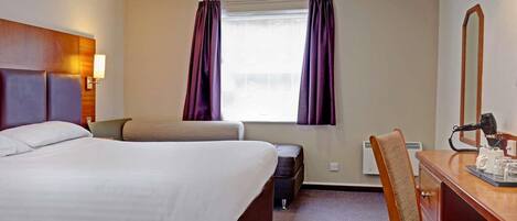 A hotel room with a bed, a desk, a chair, a window with curtains, and a mirror.