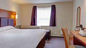 Una habitación de hotel con una cama, un escritorio con silla, un espejo y una ventana con cortinas.