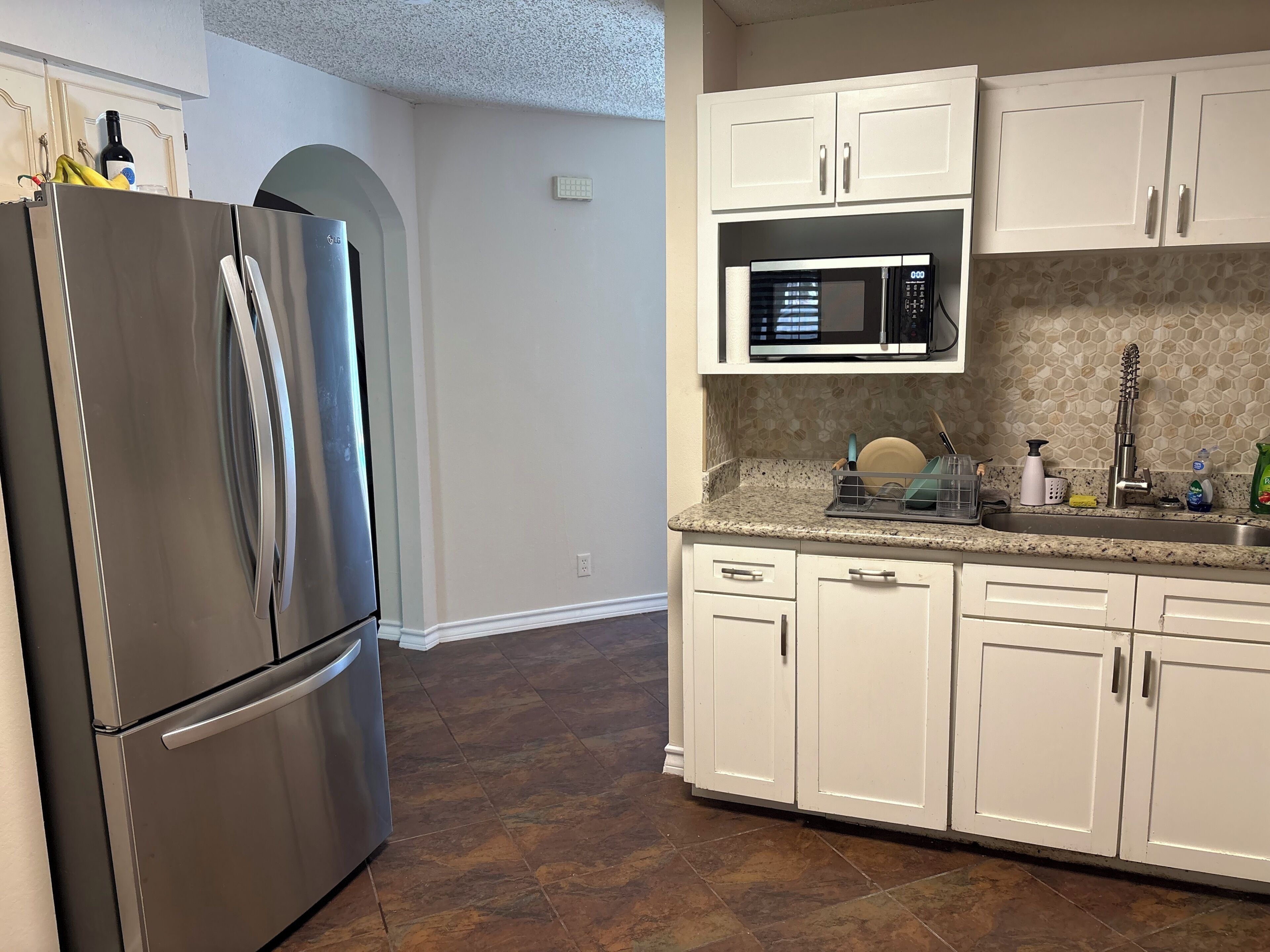 A kitchen with white cabinets, a stainless steel refrigerator, a microwave, and a tiled backsplash.