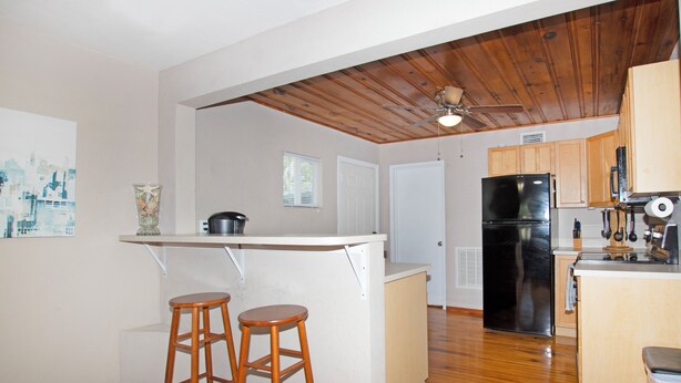 Cucina con soffitto in legno, mobili bianchi, frigorifero nero e due sgabelli di legno.