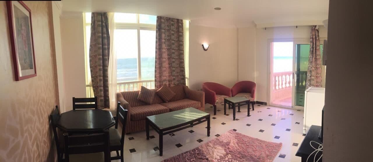 Ein Wohnzimmer mit Sofa, Couchtisch und Sesseln, einem Esstisch und Meerblick durch große Fenster.