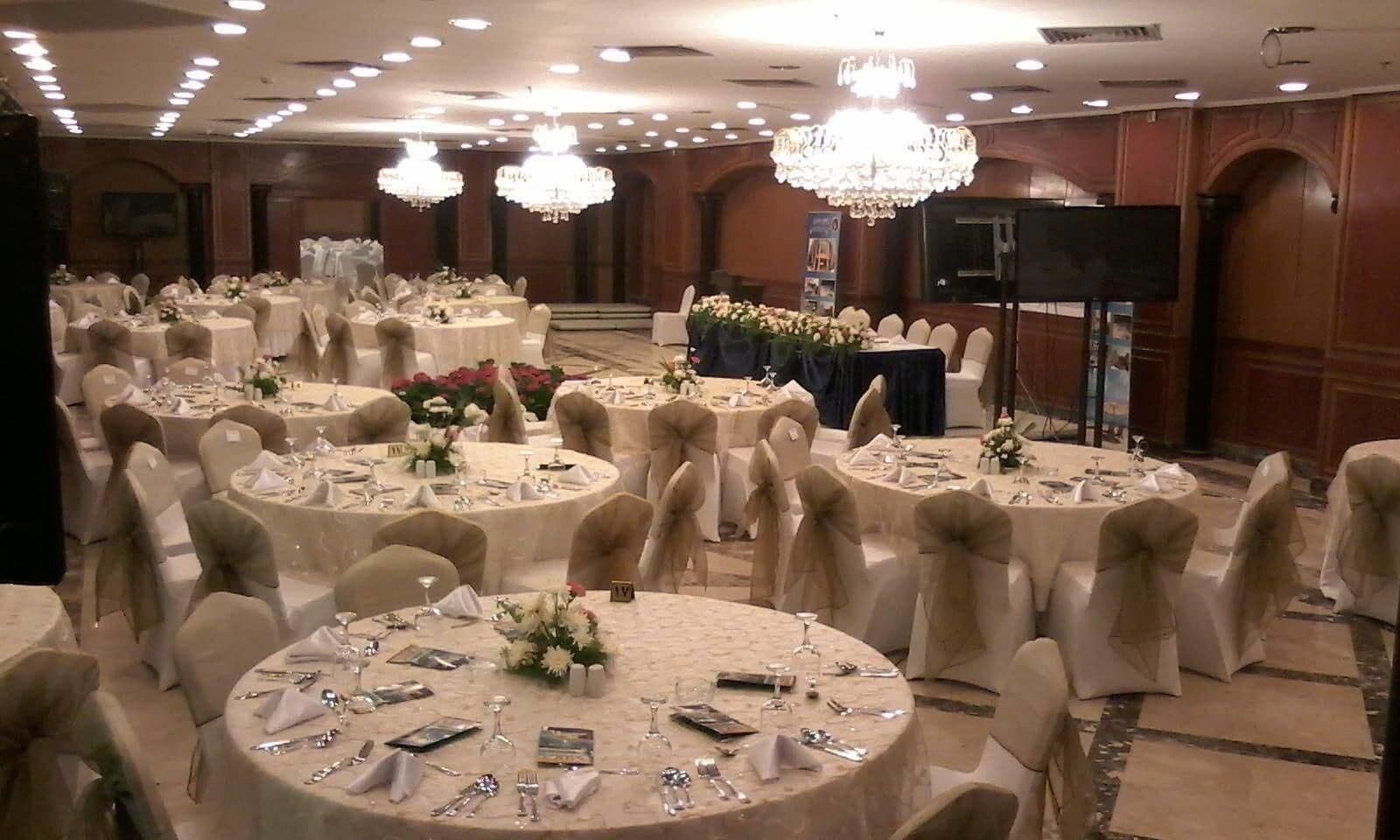 A banquet hall with round tables, chairs, and chandeliers.