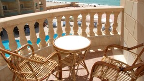 A balcony with a view of the beach and ocean, featuring wicker furniture and a small round table. - Royal Sea View (Alexandria)