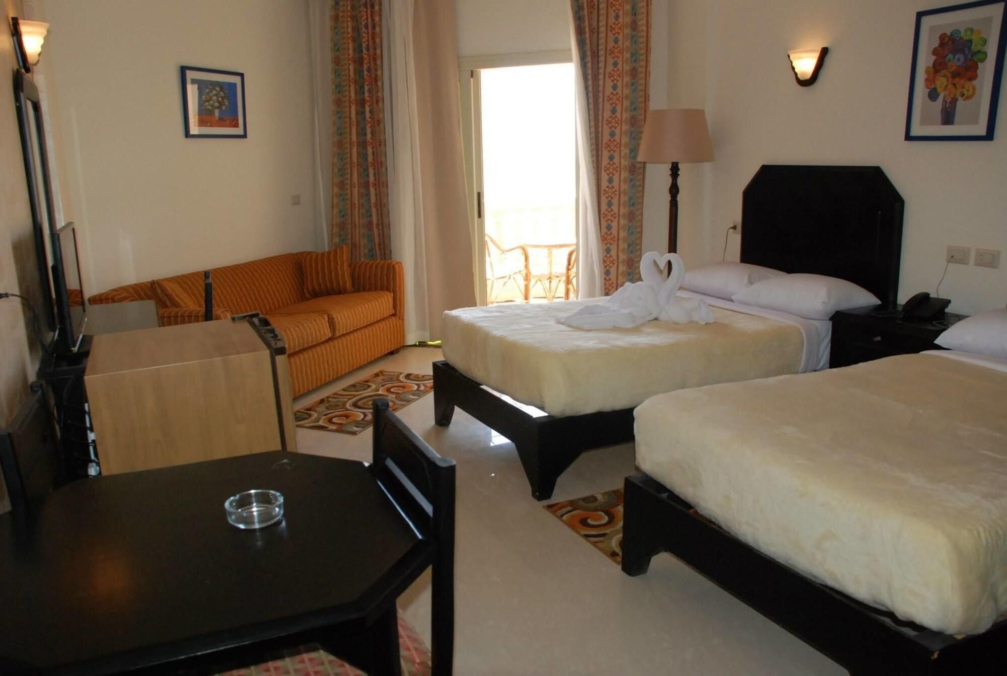 A hotel room with two beds, a sofa, a table, and a chair.