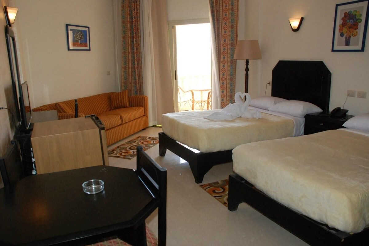 A hotel room with two beds, a sofa, a table, and a chair.