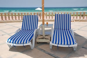 Two striped lounge chairs with a small table and a drink on it, overlooking the ocean. - Royal Sea View (Alexandria)