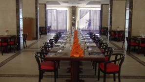 Un lungo tavolo da pranzo con sedie, un elemento decorativo arancione al centro e vista su un edificio attraverso una finestra con motivi.