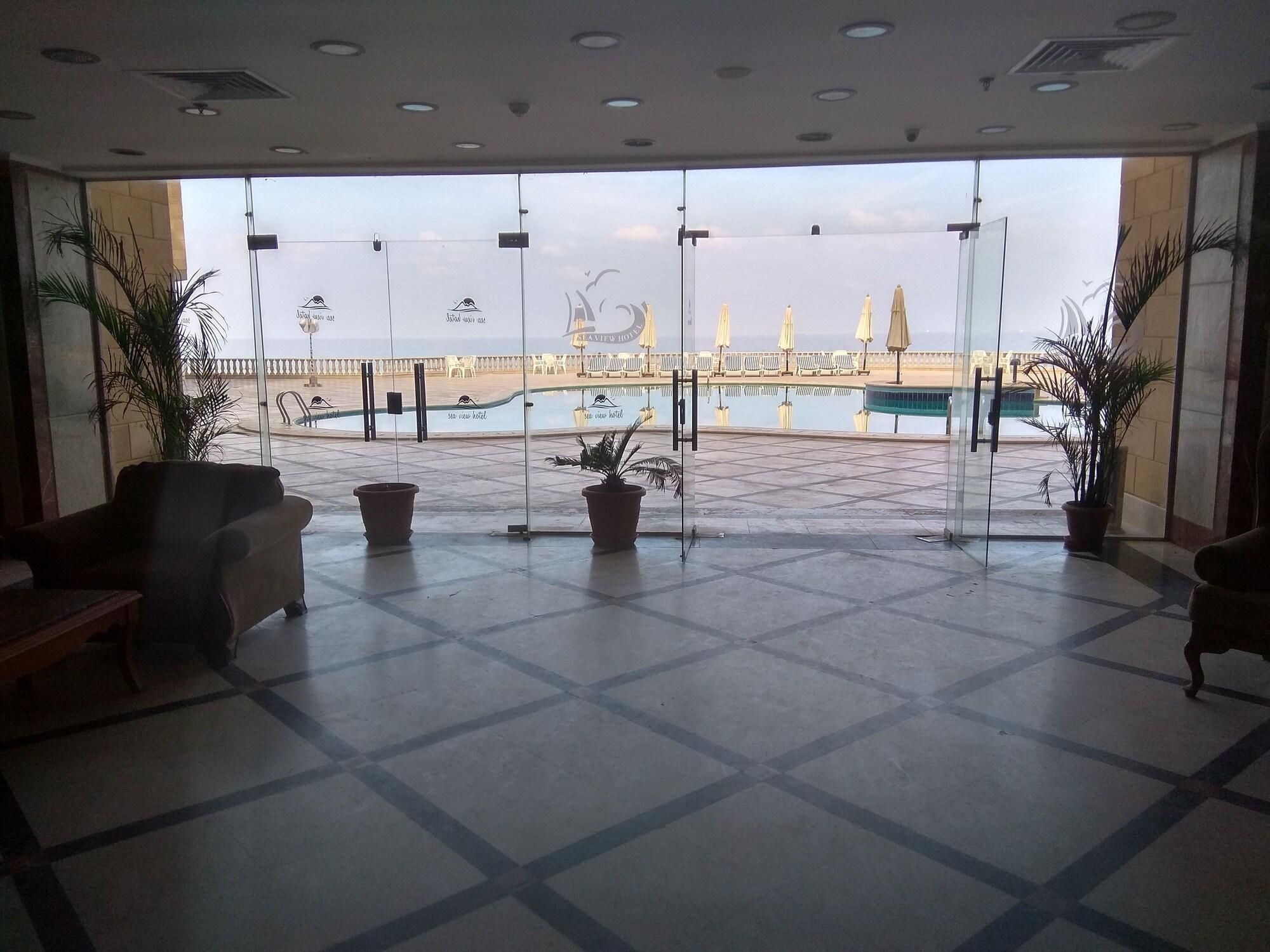 A hotel lobby with a view of a pool area, potted plants, and seating.