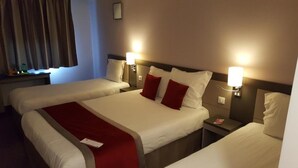 A hotel room with two beds, each with a red throw blanket, bedside lamps, and a nightstand with a lamp.