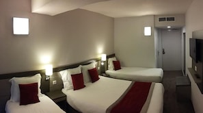 A hotel room with three beds, two bedside lamps, a TV, and a door leading to another room.