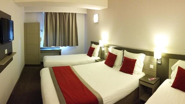 A hotel room with three beds, a television, a window with curtains, and bedside lamps.