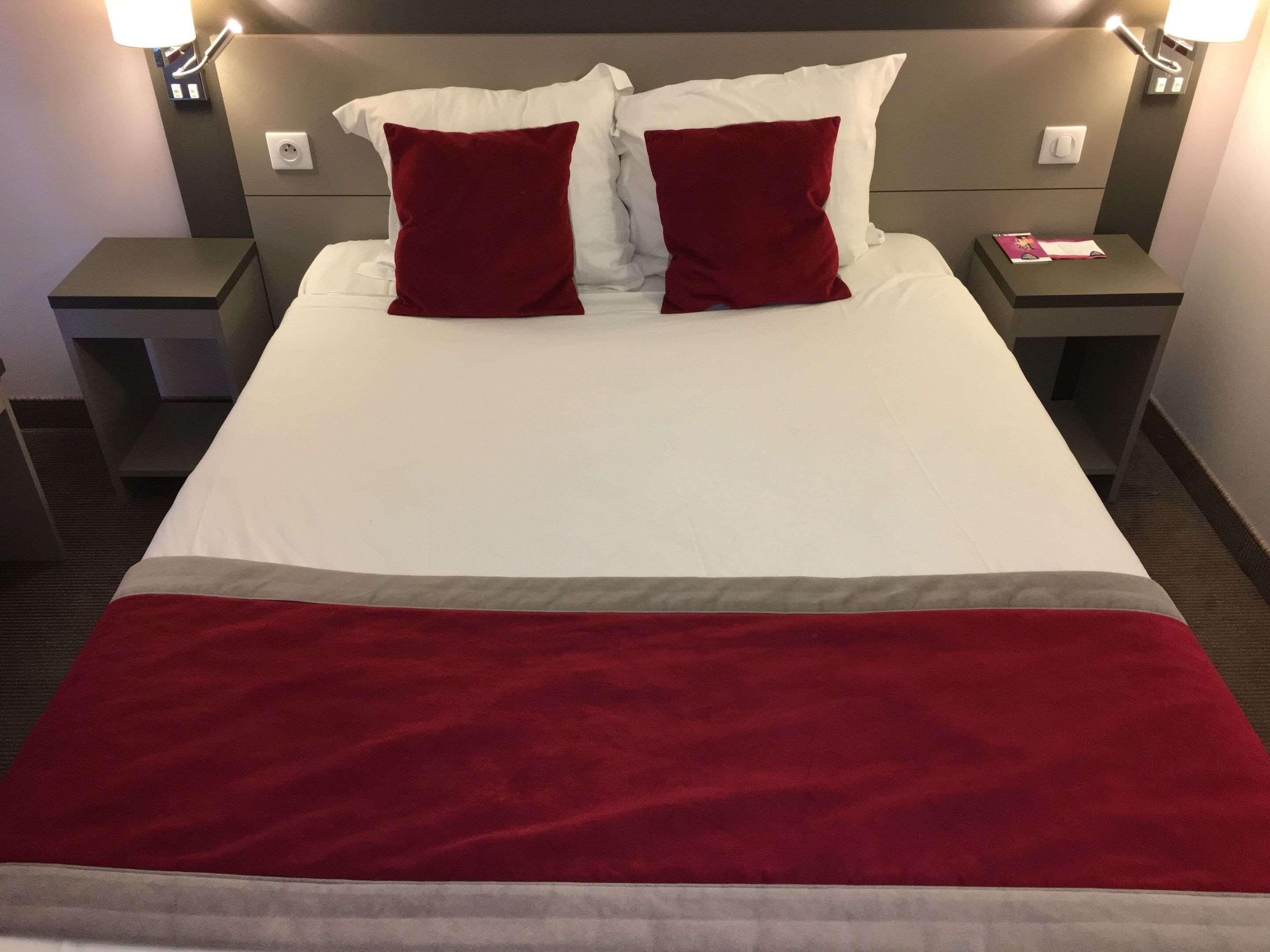 A hotel room with a bed, two nightstands, a red throw blanket, and a lamp on each nightstand.
