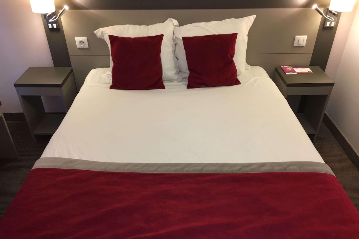 A hotel room with a bed, two nightstands, a red throw blanket, and a lamp on each nightstand.