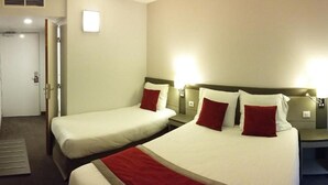 A hotel room with two beds, a bedside table, a lamp, and a door.