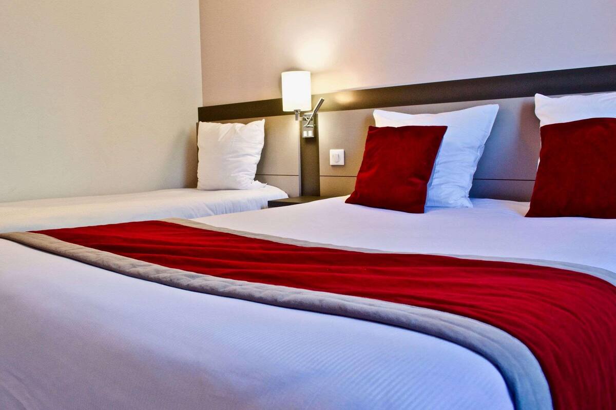 A hotel room with two beds, a nightstand with a lamp, and a red and white bedspread.