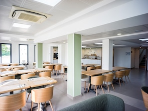 A modern cafeteria with multiple tables and chairs, a coffee station, and a staircase leading to an upper level.