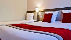 A hotel room with two beds, a nightstand with a lamp, and a red and white bedspread.
