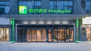 A Holiday Inn hotel entrance with a prominent green logo, large glass doors, and a modern architectural design.