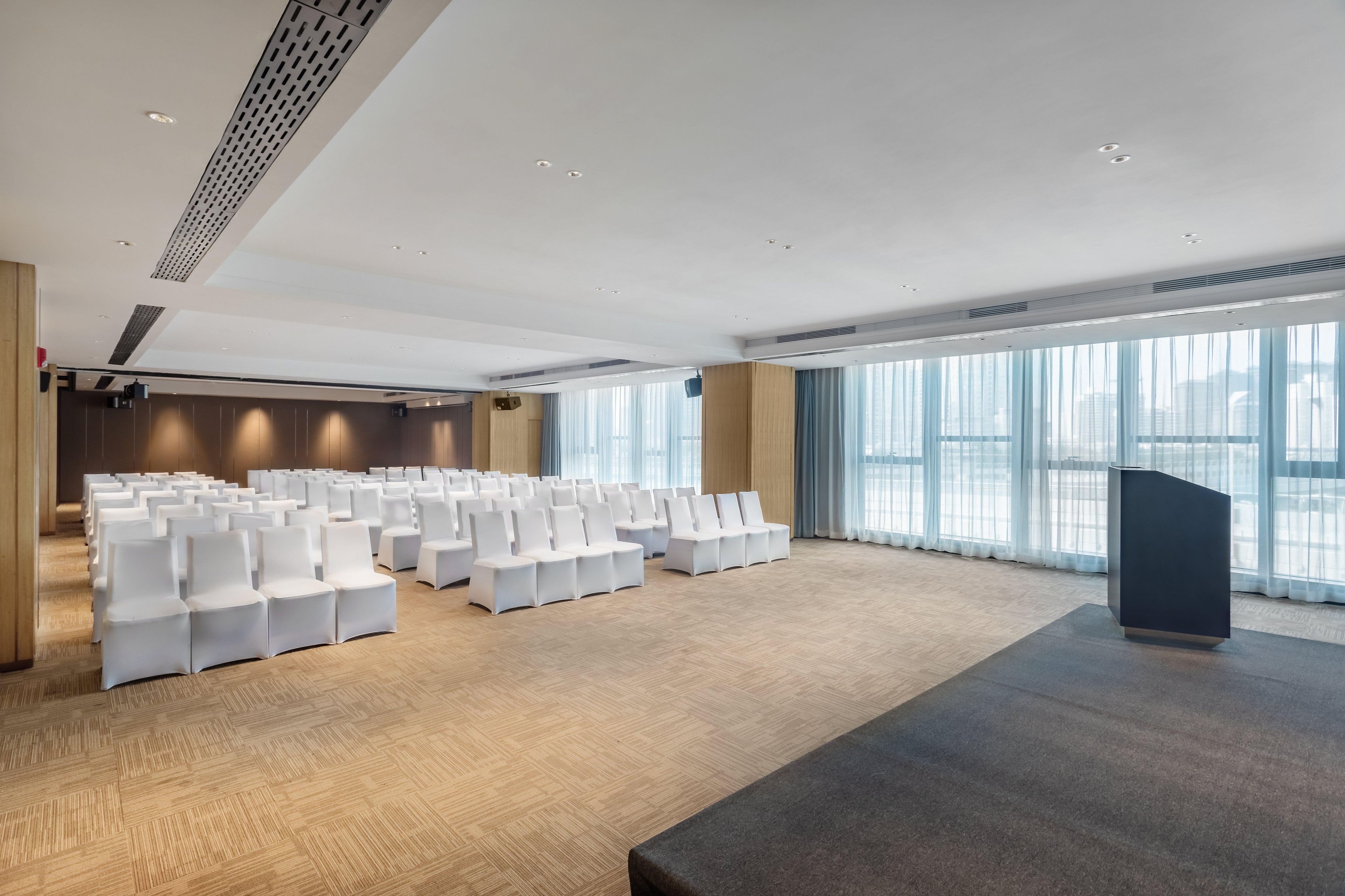 A conference room with rows of white chairs, a podium, and large windows.