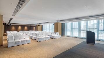 A conference room with rows of white chairs, a podium, and large windows.