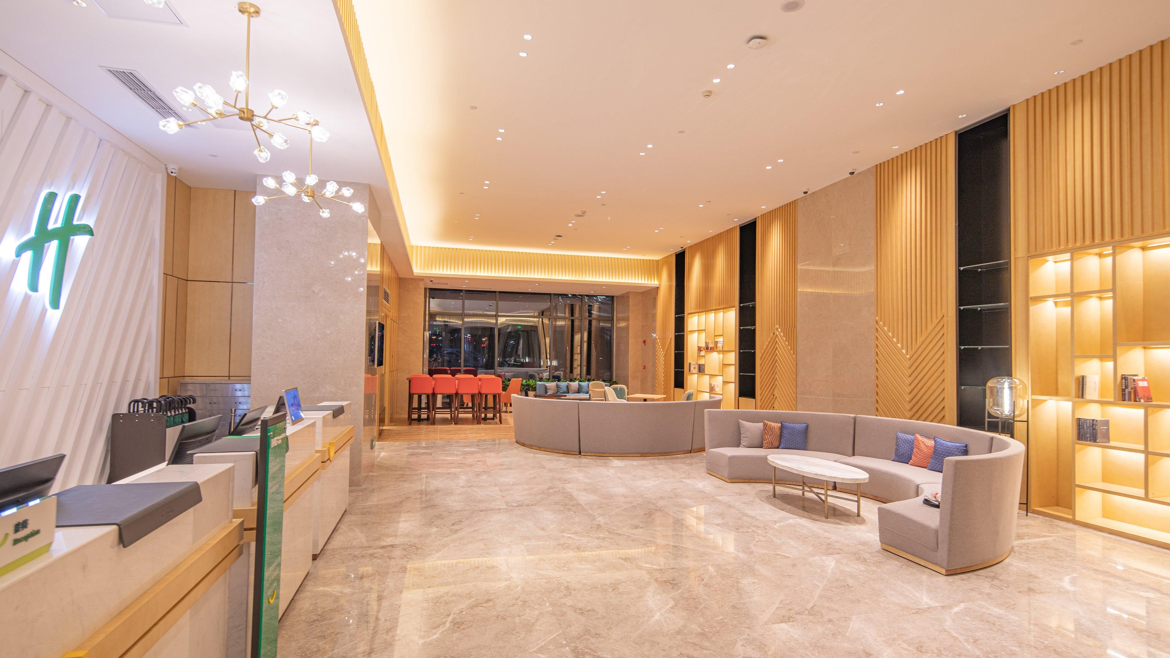 A modern hotel lobby with a reception desk, seating area, and a large window.