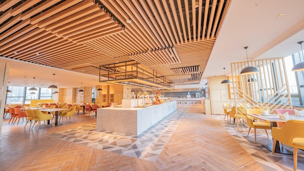 A spacious hotel lobby with a central bar area, multiple seating arrangements, and a modern ceiling design.