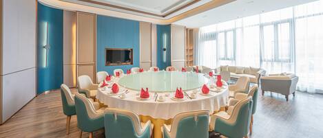 A conference room with a round table, teal chairs, and a TV mounted on the wall.