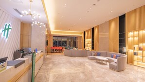 A modern hotel lobby with a reception desk, seating area, and a large window.