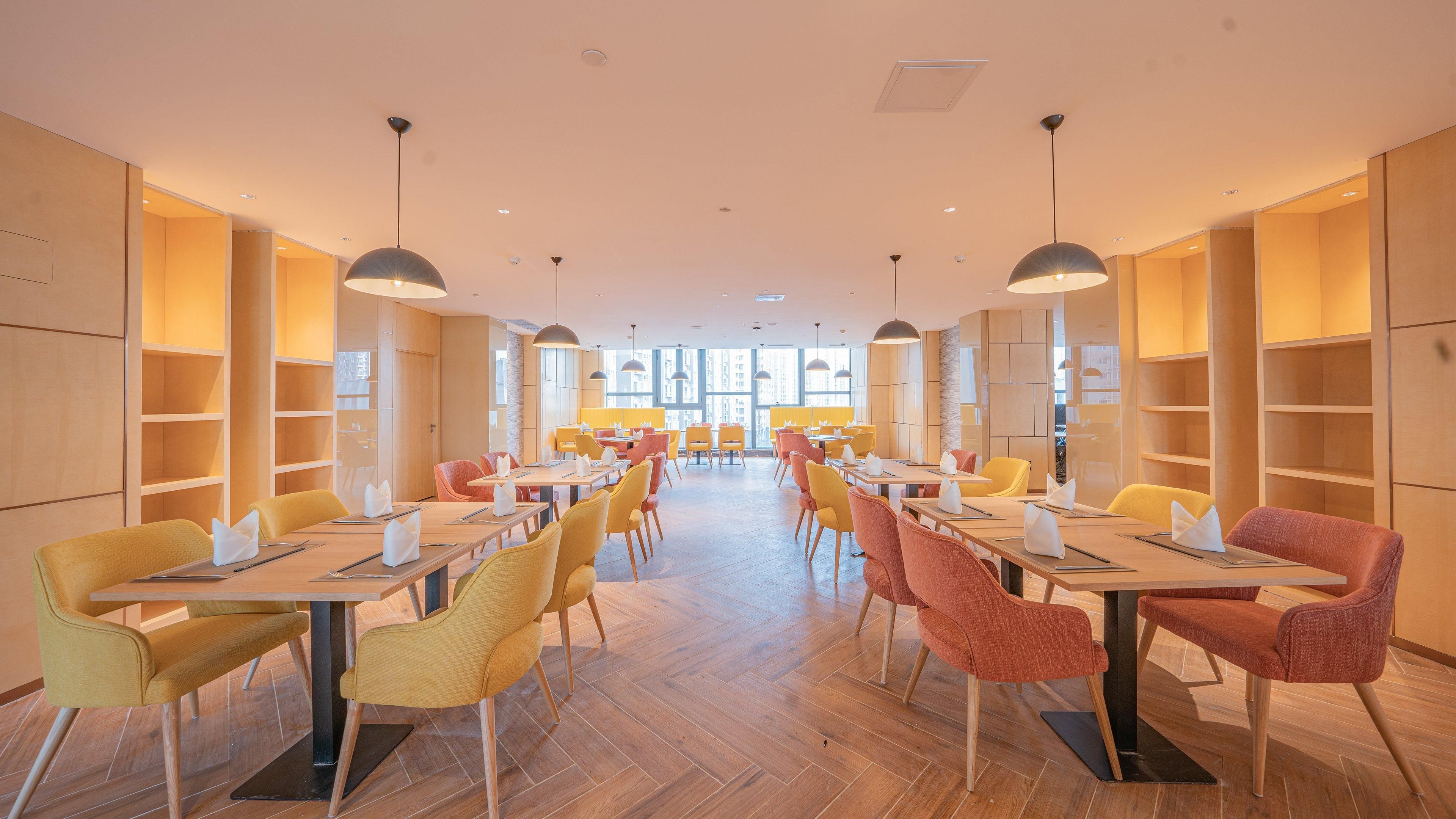 A modern restaurant with wooden floors, yellow and red chairs, and pendant lighting.